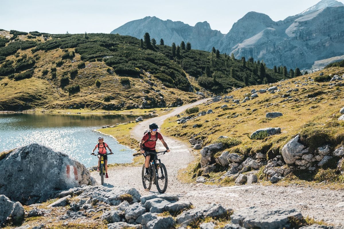 Due ciclisti in e-bike su una strada sterrata di montagna accanto a un lago